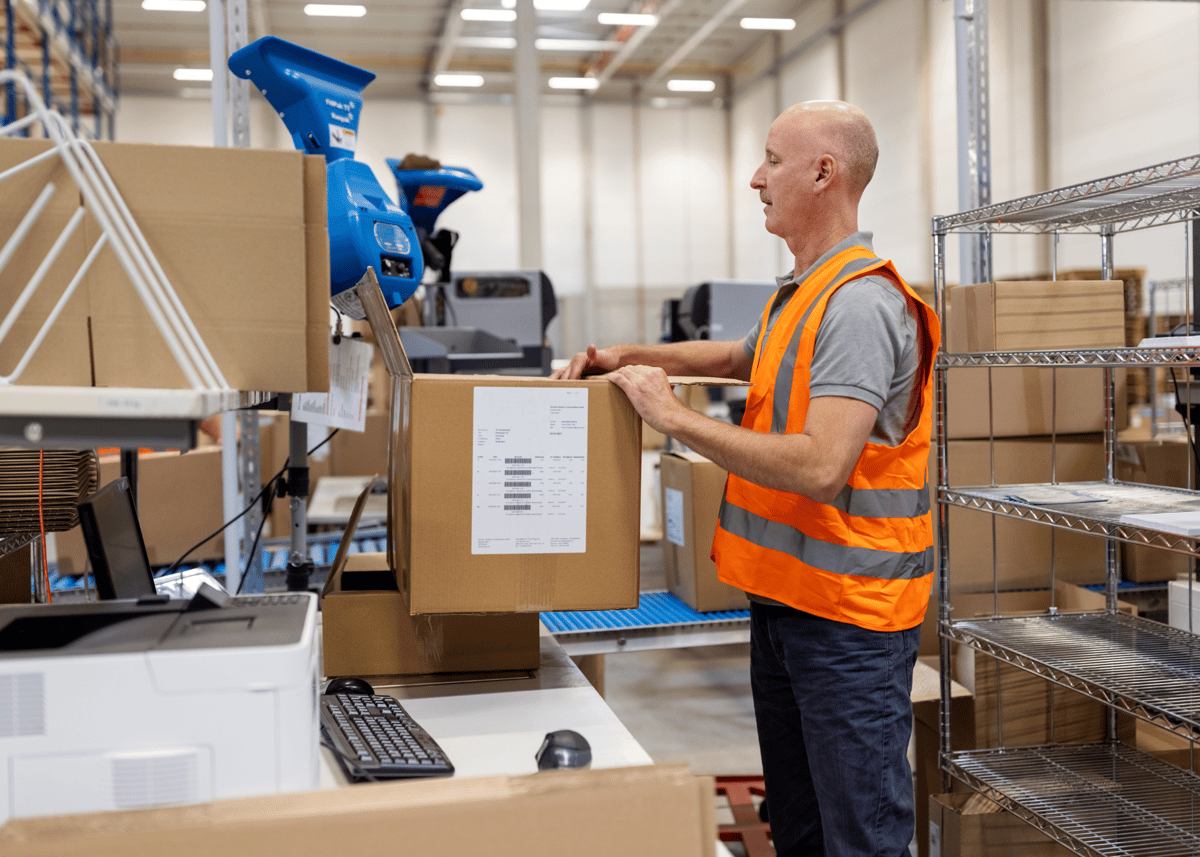 A man in an orange vest kitting the customer's product in boxes.