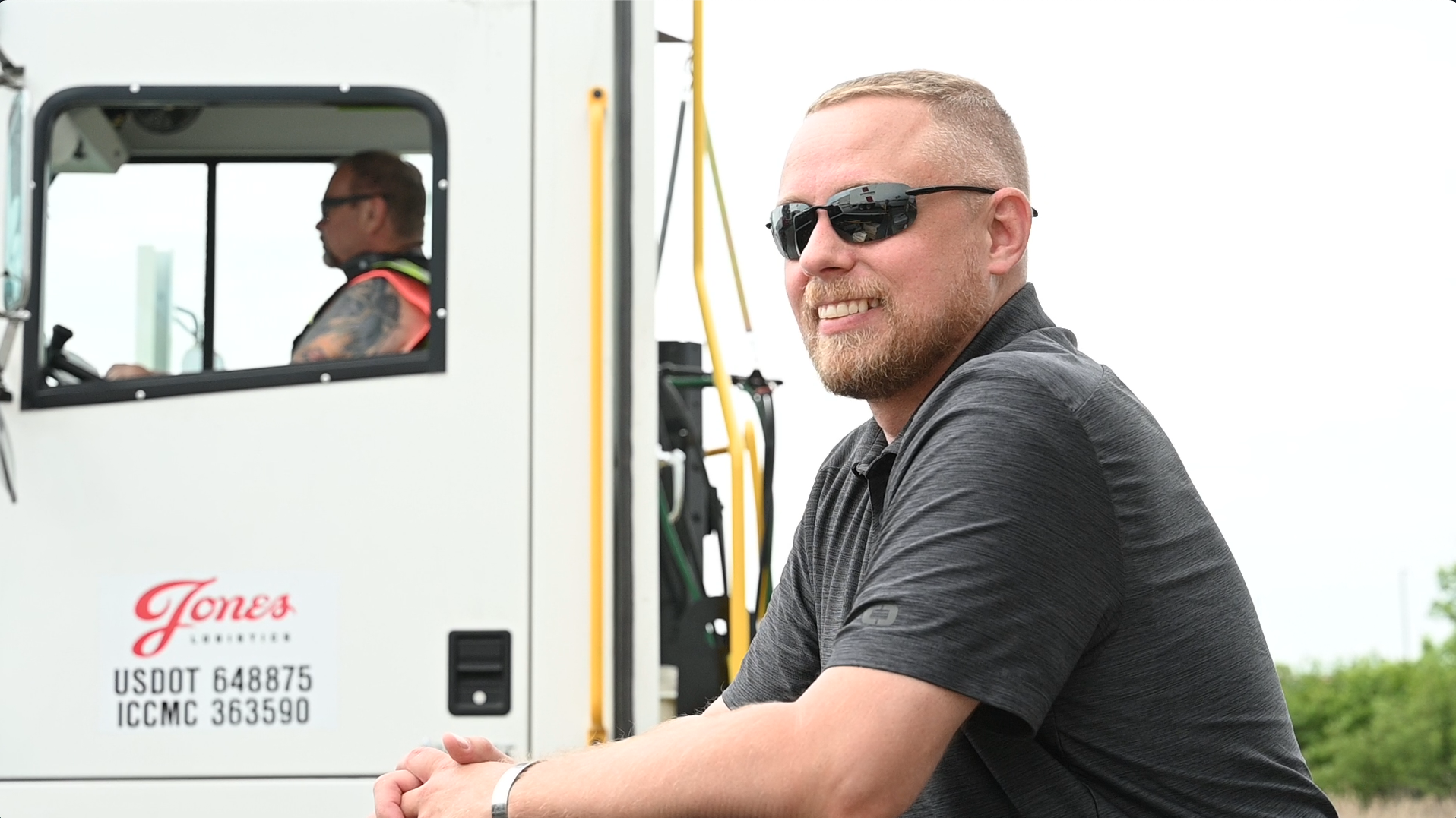 A Jones Logistics (JoLo) operations manager smiles as a JoLo spotter truck drives off behind him at a customer's facility in Wisconsin.