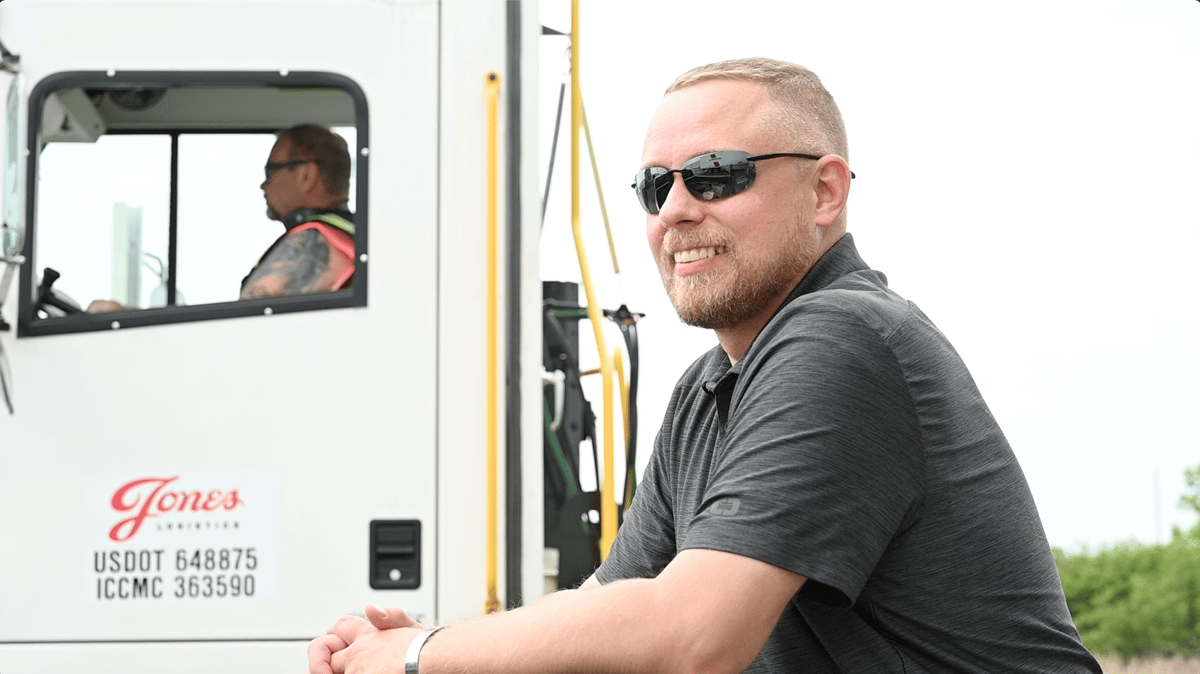 A Jones Logistics (JoLo) operations manager smiles as a JoLo spotter truck drives off behind him at a customer's facility in Wisconsin.