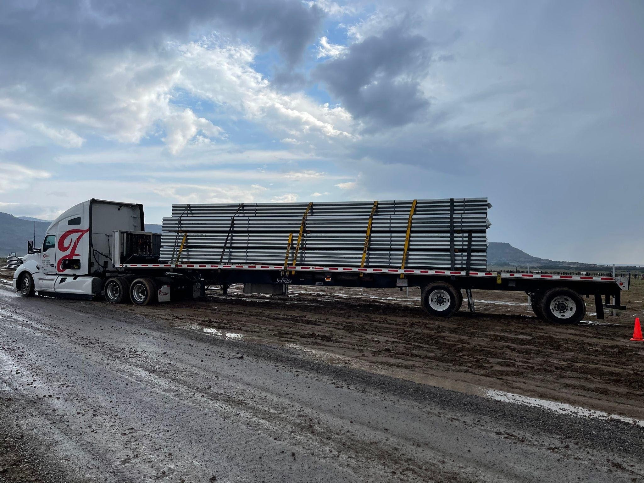 JoLo dedicated flatbed truck hauling a load of solar panel pipes.