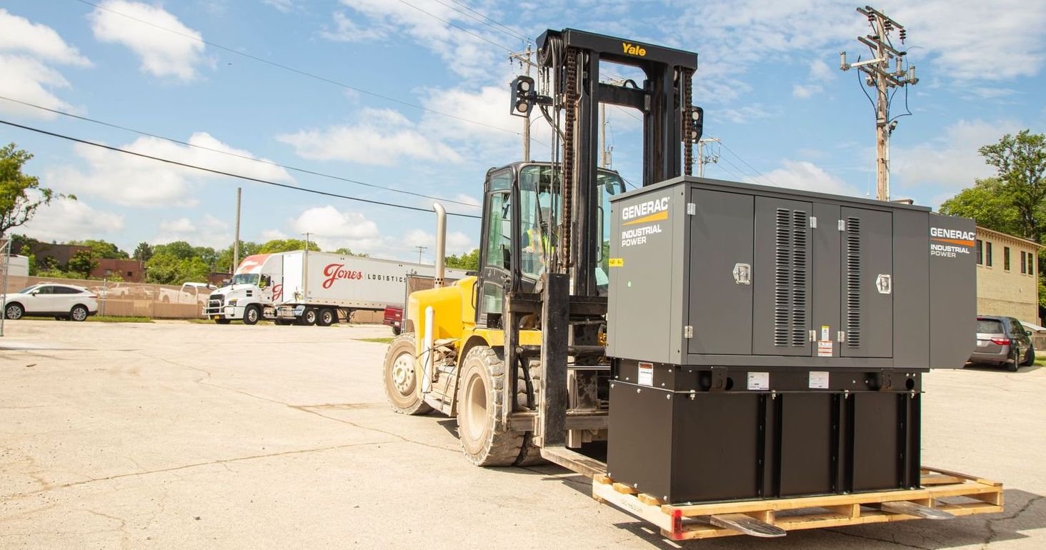 A forklift carries a generater accross a yard managed by Jones Logistics.